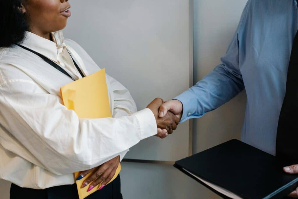 two people shaking hands while hading over documents