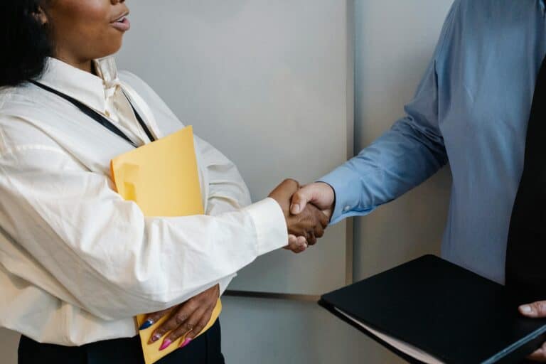 two people shaking hands while hading over documents